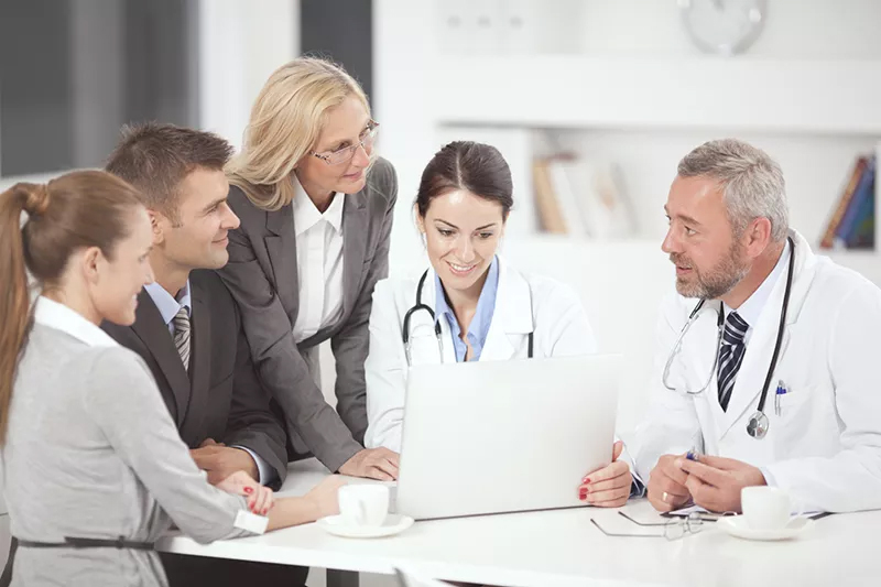A diverse group of doctors and nurses collaborating on a laptop in a medical setting